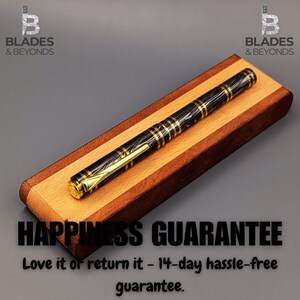 May include: A black and gold fountain pen with a patterned design rests on a wooden pen case. The pen features gold accents and a gold nib. The case is made of light and dark wood. The image includes the text "HAPPINESS GUARANTEE".