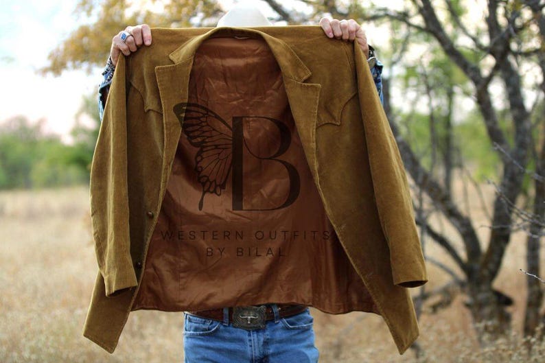 May include: A brown suede jacket with a brown satin lining. The lining features a butterfly design and the text "Western Outfits by Bilal".