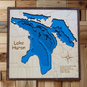 Può includere: Una mappa in legno del lago Huron, con la profondità del lago rappresentata in sfumature di blu. Il testo "Lake Huron" è visibile. La mappa include una rosa dei venti e dettagli sulla superficie, la profondità e le dimensioni del lago in miglia e piedi.