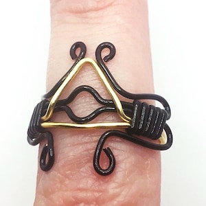 May include: A black and gold wire ring with a triangular design. The ring is made of wire that has been twisted and shaped into a geometric pattern.