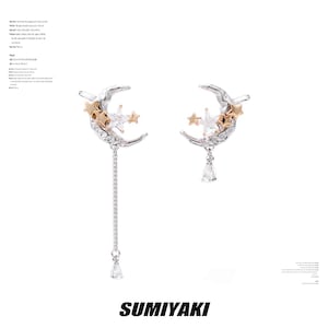 Könnte beinhalten: Silberfarbene Ohrringe mit einem Mond-Design, goldfarbenen Sternen und klaren Kristallakzenten. Ein Ohrring hat eine Kette mit einem tropfenförmigen Kristall. Das Wort "SUMIYAKI" ist unten aufgedruckt.