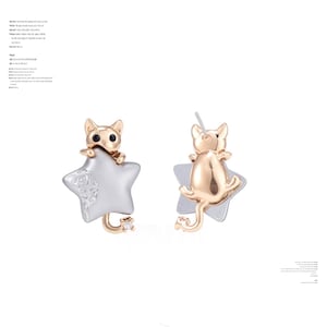 May include: A pair of cat-shaped earrings. Each earring features a gold-colored cat perched on a silver star. The cat has black eyes and a tail. The star has a decorative pattern. A small, clear gem is at the end of the cat's tail.