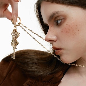 May include: A gold-toned metal keychain featuring a circular ring attached to a delicate chain and a cluster of ornate, vintage-style skeleton keys with intricate detailing. The word SUMIYAKI is printed in white at the bottom of the image.