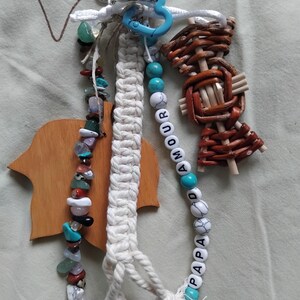 May include: A selection of handmade keyrings. One keyring has a macrame design, another features a beaded strand with the word "AMOUR PAPA", and a third is made of woven wood. The keyrings are attached to a silver clasp and a blue heart-shaped ring.