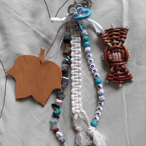 May include: A selection of handmade keyrings and charms. Features a wooden leaf, a woven basket, and beaded strands with turquoise, white, and colourful stones. One keyring spells "PAPA AMOUR" with white letter beads and turquoise accents.