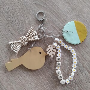 May include: A wooden bird charm with a small leaf charm, a woven bow charm, a daisy bead charm bracelet that spells "NATURE", and a round, two-toned paper charm with a light blue and yellow color scheme.