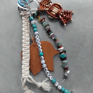 May include: A selection of keychains and accessories. Features a macrame keychain, a beaded keychain with the word "AMOUR" and a wooden charm. Also includes a woven bow and a keychain with various colourful stones.