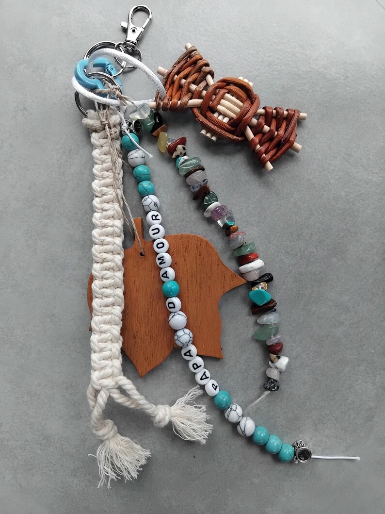 May include: A selection of keychains and accessories. Features a macrame keychain, a beaded keychain with the word "AMOUR" and a wooden charm. Also includes a woven bow and a keychain with various colourful stones.
