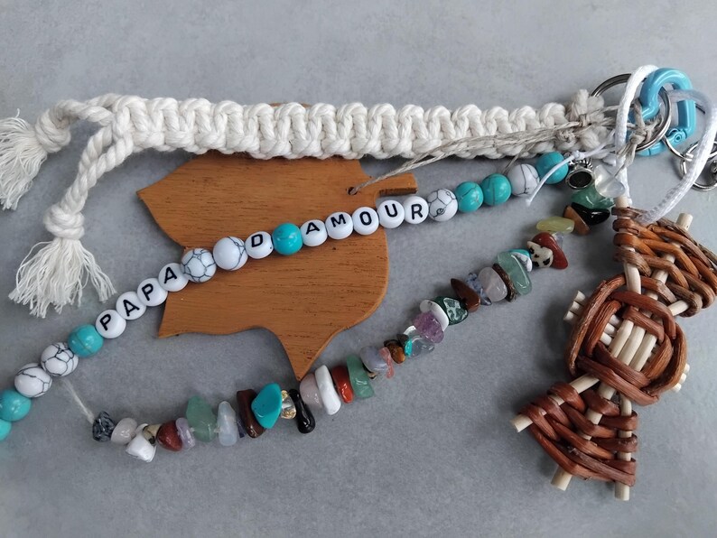 May include: A selection of handmade keychains and accessories. Features a macrame keychain, a beaded keychain with the text "PAPA AMOUR", a gemstone beaded keychain, and a woven figure keychain. The items are in various colours.