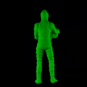 Pu&ograve; includere: Figurina di azione in plastica verde di un mostro con una texture squamosa. La figura &egrave; in piedi con le braccia lungo i fianchi e le gambe leggermente divaricate.