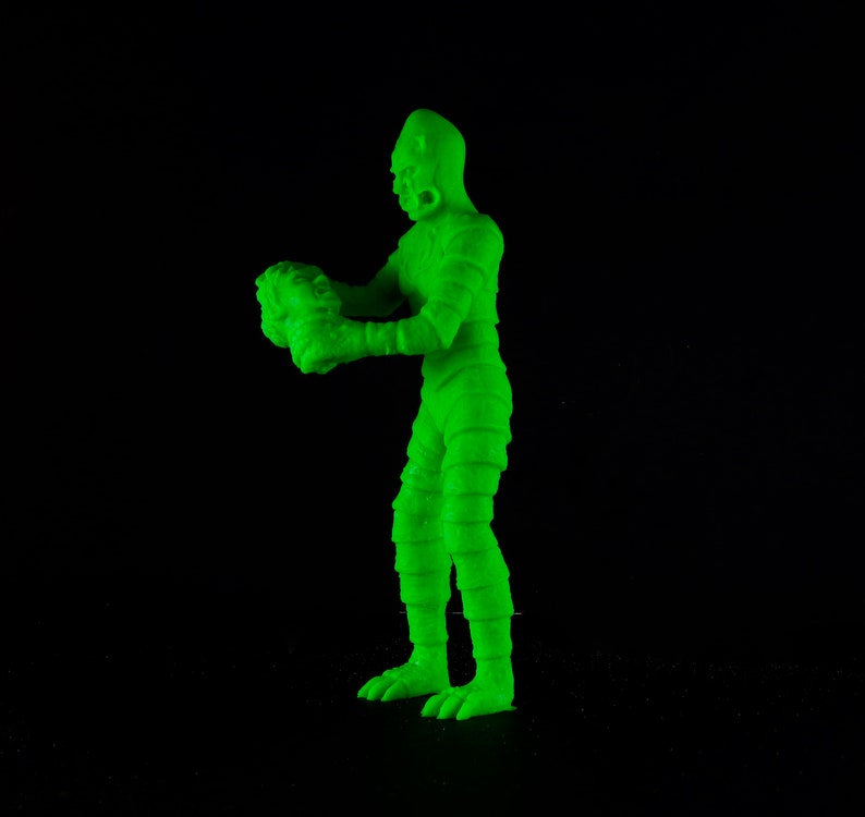 Pu&ograve; includere: Una figura di plastica verde di un mostro che tiene una testa pi&ugrave; piccola nelle sue mani. Il mostro ha un corpo squamoso e testurizzato e una grande testa con una bocca larga.