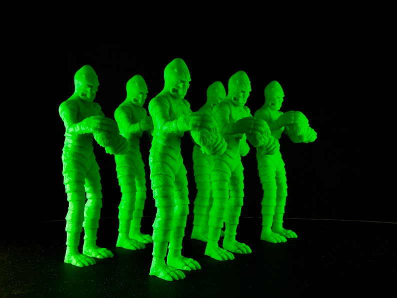 Pu&ograve; includere: Cinque figure di plastica verde di una creatura di un film horror. Le figure sono in piedi in fila, rivolte in avanti. Hanno tutte la stessa posa, con le braccia alzate e le mani chiuse a pugno.