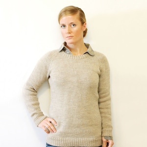 Puede incluir: Un suéter de punto beige con cuello redondo y mangas largas.