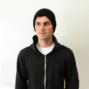 May include: A man wearing a black knit beanie and a black zip-up hoodie.