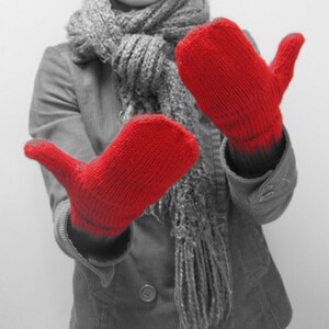 May include: A person wearing a gray scarf and a pair of red knitted mittens. The mittens are held out in front of the person, with the palms facing outward.