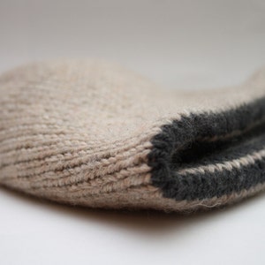 May include: A beige knitted hat with a black trim. The hat is folded in half and the trim is visible on the outside.