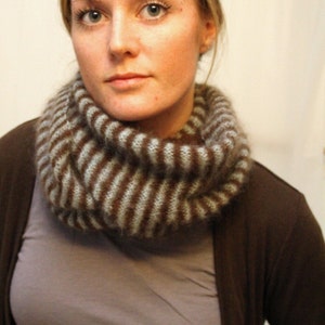 May include: A woman wearing a brown cardigan and a gray and brown striped infinity scarf.