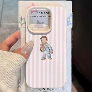 May include: A phone case with a pink and white striped pattern. The case features a cartoon illustration of a boy in pajamas holding a teddy bear. The text "STAR" and "HAPPINESS IS THE MOST IMP" is visible on the case.