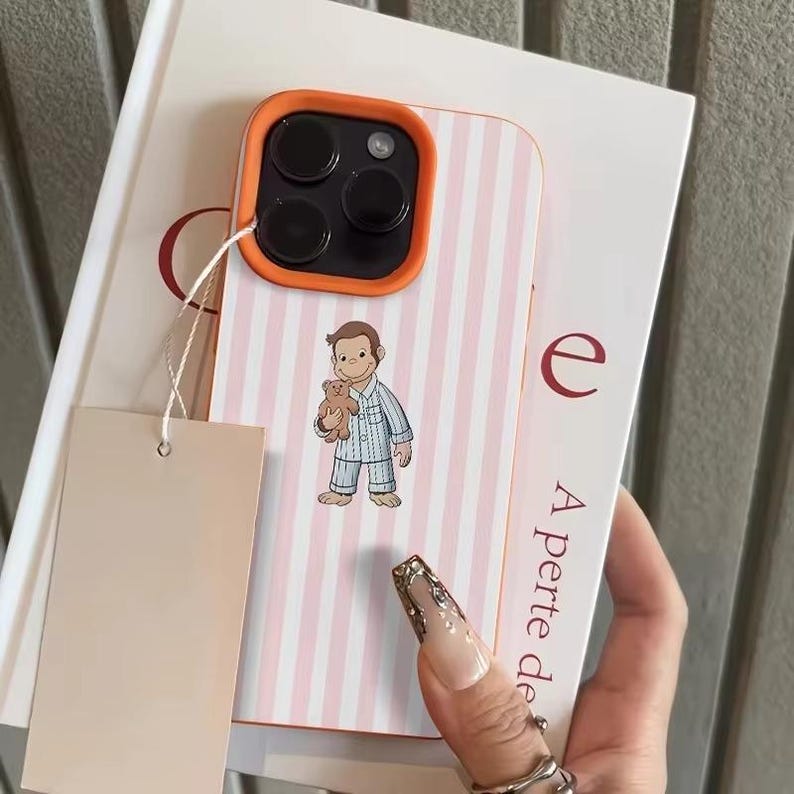 May include: A phone case with a pink and white striped pattern and an orange border. The case features a cartoon illustration of a character in pajamas holding a teddy bear. A blank tag is attached.