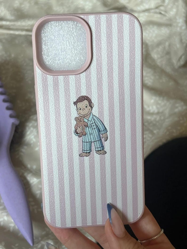 May include: Pink and white striped phone case featuring a cartoon illustration of a monkey in pajamas holding a teddy bear. The case has a pink border around the camera cutout and a matching pink border. The case is designed for a smartphone.