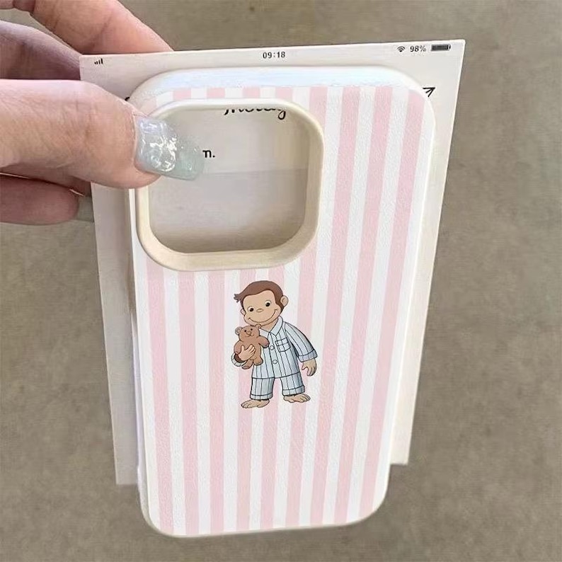 May include: A pink and white striped phone case featuring a cartoon illustration of a boy in pajamas holding a teddy bear. The case has a light beige border around the camera cutout.