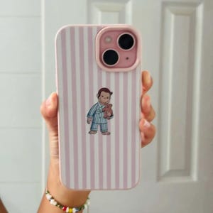 May include: Pink and white striped phone case with a cartoon illustration of a character in pajamas holding a teddy bear. The case has a pink camera module and a matching pink border.