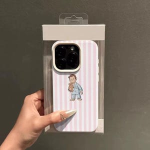 May include: A phone case with a pink and white striped pattern. The case features an illustration of a cartoon character holding a teddy bear. The case is in a clear plastic package.