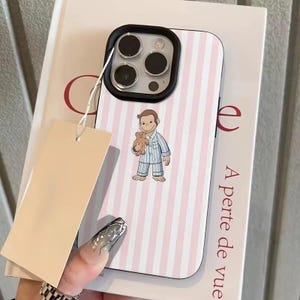 May include: A phone case with a pink and white striped pattern. The case features a cartoon illustration of a character in pajamas holding a teddy bear. The phone case has a black border around the camera.
