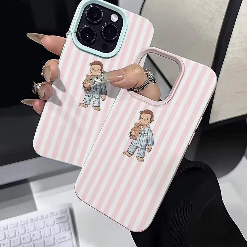 May include: Two phone cases with a pink and white striped pattern. Each case features a cartoon illustration of a boy in pajamas holding a teddy bear. The cases have a light blue and pink border.
