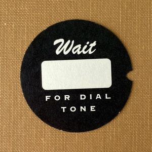 May include: Black and white round sticker with the text "Wait for dial tone" and a blank space for a phone number.