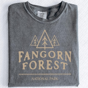 May include: A dark gray t-shirt with a vintage look featuring a graphic of three stylized pine trees and the text "Fangorn Forest National Park".
