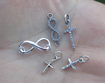 May include: Four silver charms, two infinity symbols and two crosses, all with clear crystal accents.