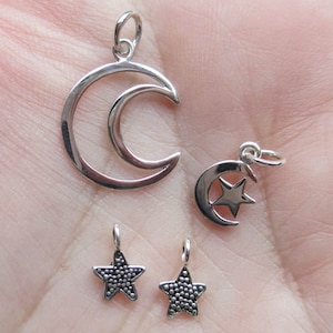 May include: Four silver charms: a crescent moon, a crescent moon with a star inside, and two small stars. The stars have a textured surface.
