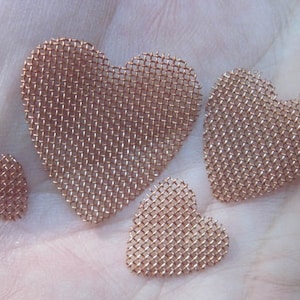 May include: Four copper mesh heart shapes of varying sizes. The largest heart is in the centre of the image, with two smaller hearts to the left and right of it. The smallest heart is at the bottom of the image.
