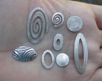 May include: A collection of nine silver metal charms with various geometric and abstract designs. The charms are small and delicate, with intricate details.