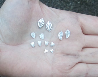 May include: A collection of silver leaf and heart shaped earrings. The earrings are arranged on a hand.