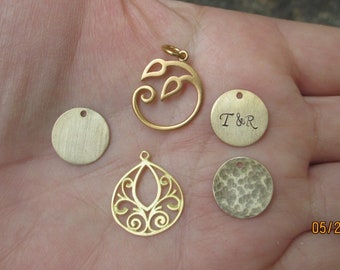 May include: Five gold-colored metal charms, including a leaf design, a teardrop shape with a filigree pattern, and three round charms. One round charm is blank, one has a hammered texture, and one is engraved with "T&R".