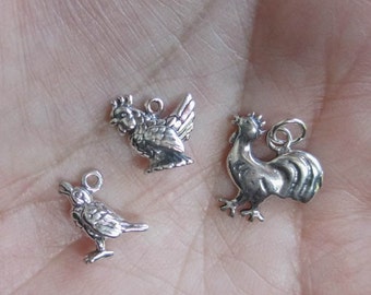May include: Three silver charm pendants in the shape of a rooster, a hen, and a bird. The charms are detailed and have a rustic look.