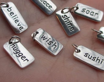 May include: Silver charm tags with various words engraved on them, including "believe", "shine", "soar", "wish", "hugger", and "sushi".