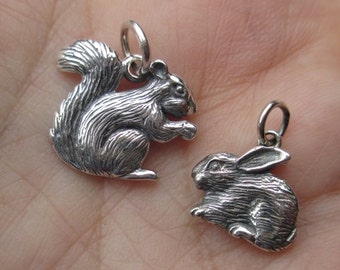 May include: Two silver charms, one of a squirrel and one of a rabbit. Both charms are detailed and have a realistic appearance.