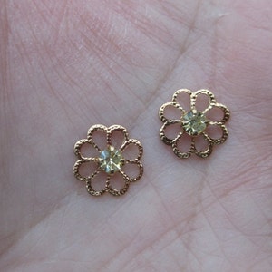 May include: Two gold-tone metal flower-shaped embellishments with clear rhinestones in the center.