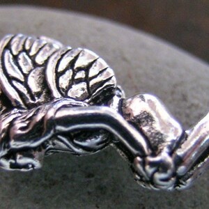 May include: A silver charm in the shape of a kneeling angel with wings. The angel has a detailed face and wings.