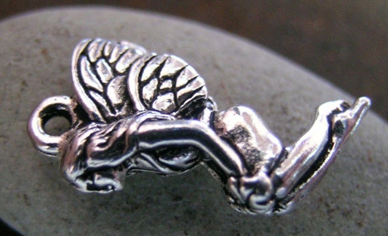 May include: A silver charm in the shape of a kneeling angel with wings. The angel has a detailed face and wings.