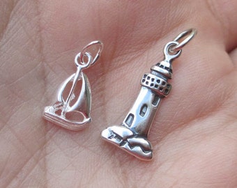 May include: Two silver charm pendants, one shaped like a sailboat and the other like a lighthouse. Both charms have a loop at the top for attaching to a bracelet or necklace.