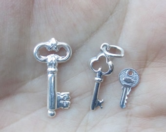 May include: Three silver key charms, one with a traditional ornate design, one with a heart-shaped bow, and one with a simple round design.