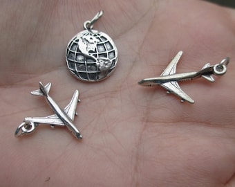May include: Three silver charm pendants: a globe, a small airplane, and a larger airplane. The charms are on a white background.