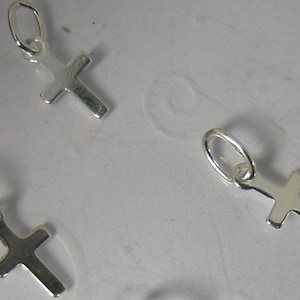 May include: Three silver cross charms with jump rings. The charms are small and delicate.