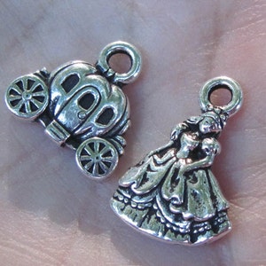 May include: Two silver charm pendants, one depicting a princess in a gown and the other a carriage. Both charms have a loop for attaching to a necklace or bracelet.