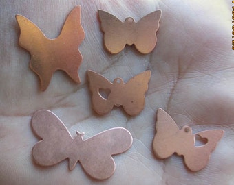 May include: Five copper-colored butterfly charms in various designs. Some have heart-shaped cutouts, and all have small holes for stringing. The charms are displayed on a light-colored surface.