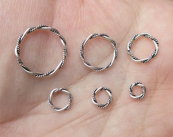 May include: Six silver rings with a twisted rope design. The rings are different sizes and are arranged in a row on a hand.